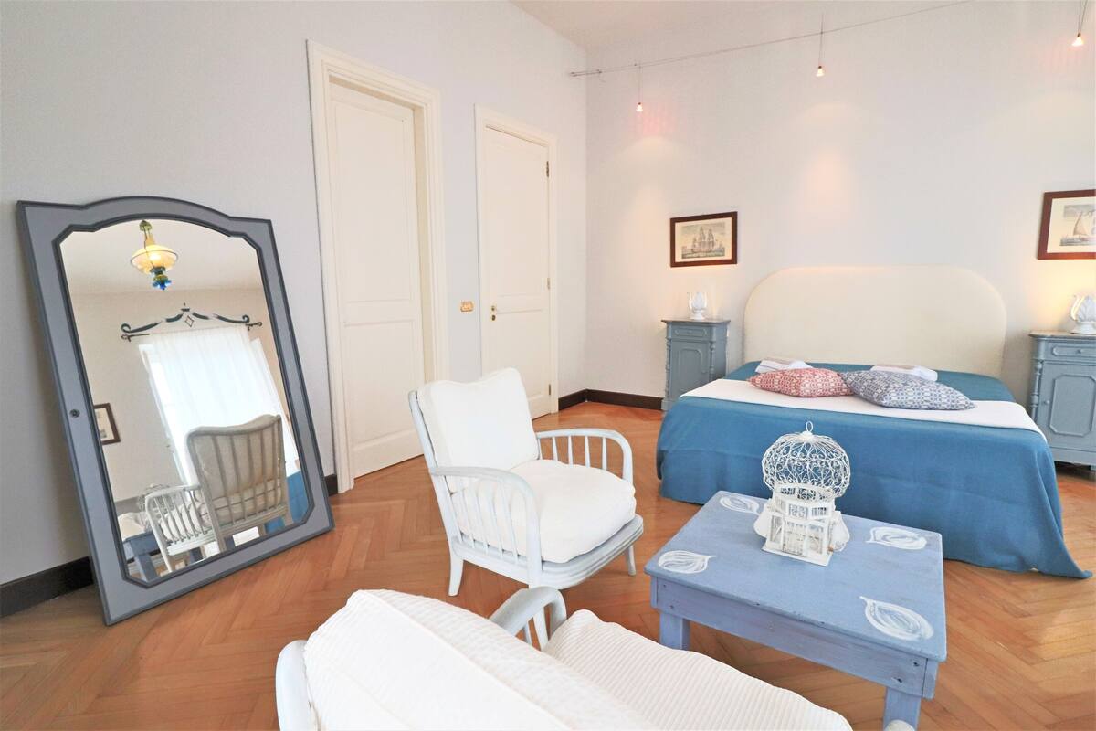 A bedroom with a bed, a chair, a table, and a mirror.