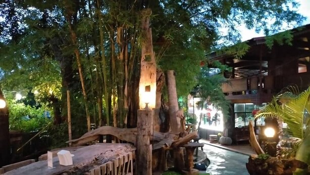 An indoor garden with a wooden bridge, artificial grass, and a large tree trunk with a light fixture. - Denchai City Resort (Den Chai)