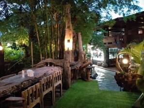 An indoor garden with a wooden bridge, artificial grass, and a large tree trunk with a light fixture. - Denchai City Resort (Den Chai)