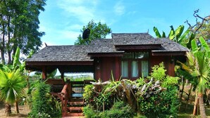 A traditional wooden house with a tiled roof, surrounded by lush greenery and banana plants. - Denchai City Resort (Den Chai)