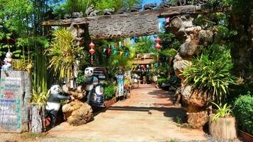 A pathway leading through a garden with panda statues, a wooden archway, and a signboard with directions.