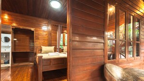 A wooden cabin interior with a bed, a wooden bench, and a window with a view of greenery. - Denchai City Resort (Den Chai)