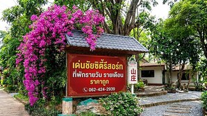 A sign with Thai text and a contact number, surrounded by lush greenery and a pathway. - Denchai City Resort (Den Chai)