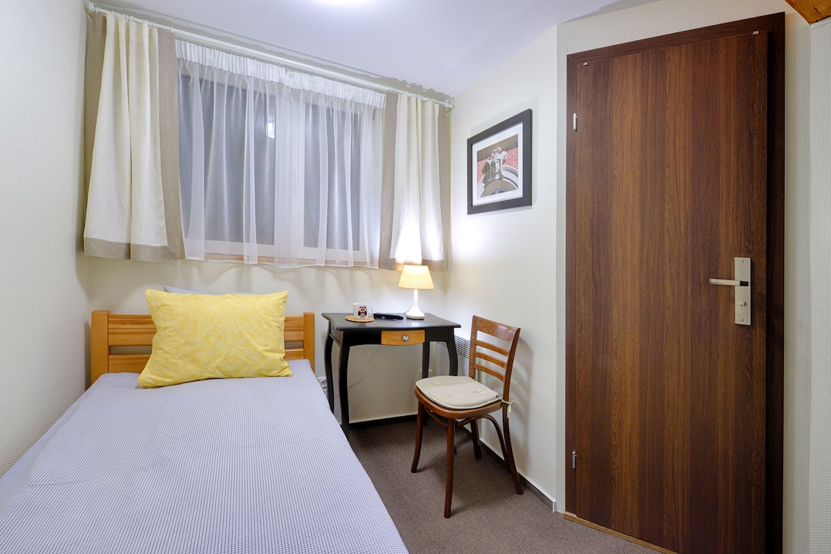 Une chambre à coucher comprenant un lit, un bureau, une chaise, une lampe, une fenêtre avec des rideaux et une porte.