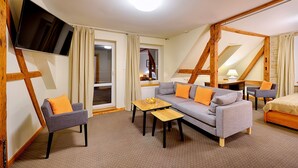 A modern hotel room with a sofa, armchair, and a flat-screen TV mounted on the wall.