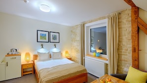 A bedroom with a bed, bedside tables, a small desk, a window with curtains, and a view of the outside.