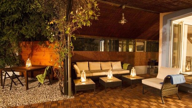 An outdoor patio with a wooden floor, a sofa, two armchairs, and a table with lanterns.
