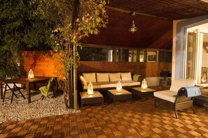 Une terrasse extérieure dotée d’un plancher en bois, d’un canapé, de deux fauteuils et d’une table agrémentée de lanternes.