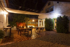 Eine Terrasse im Freien mit Tischen und Stühlen, einem überdachten Bereich und einem Hauseingang.