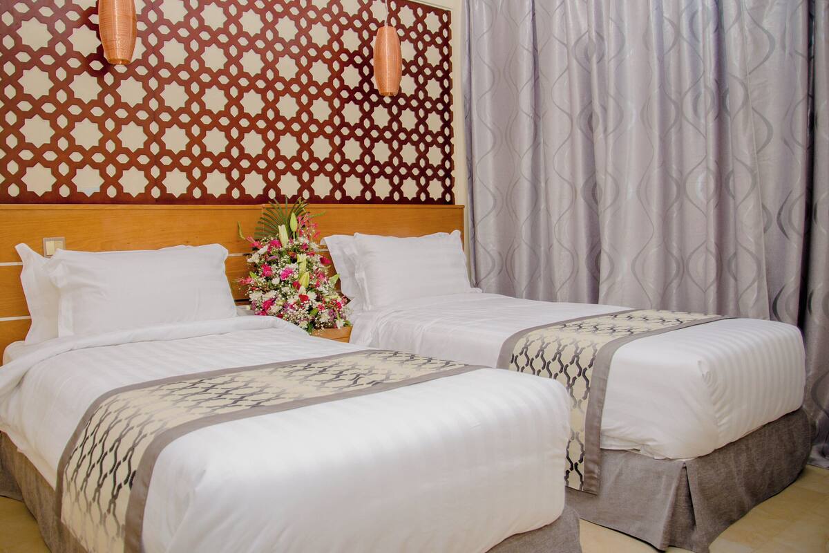 A hotel room with two beds, a decorative wall, and a curtain.