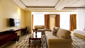 A hotel room with a flat-screen TV, a sofa, a coffee table, a dining table, and a bed. - Saab Royale Hotel (Nairobi)