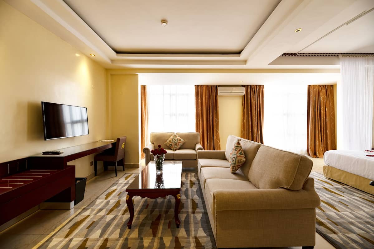 A hotel room with a flat-screen TV, a sofa, a coffee table, a dining table, and a bed.