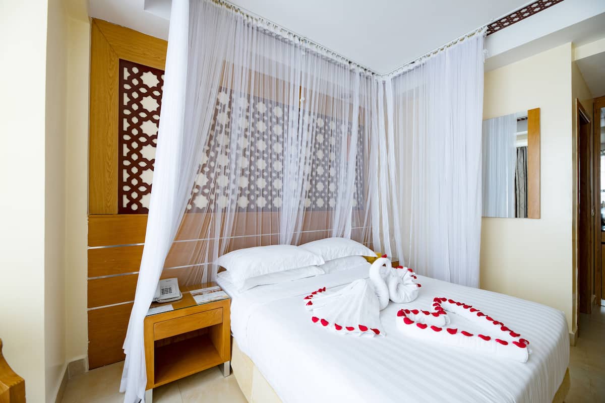 A hotel room with a bed, a wooden nightstand, a telephone, and a decorative partition.