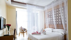 A hotel room with a bed, a TV, a chair, a desk, and a vase with flowers. - Saab Royale Hotel (Nairobi)