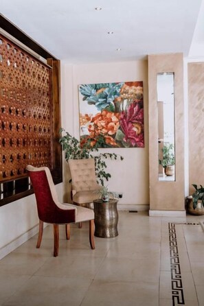 A room with a wooden partition, a red chair, a beige chair, a potted plant, and a large floral painting on the wall. - Saab Royale Hotel (Nairobi)