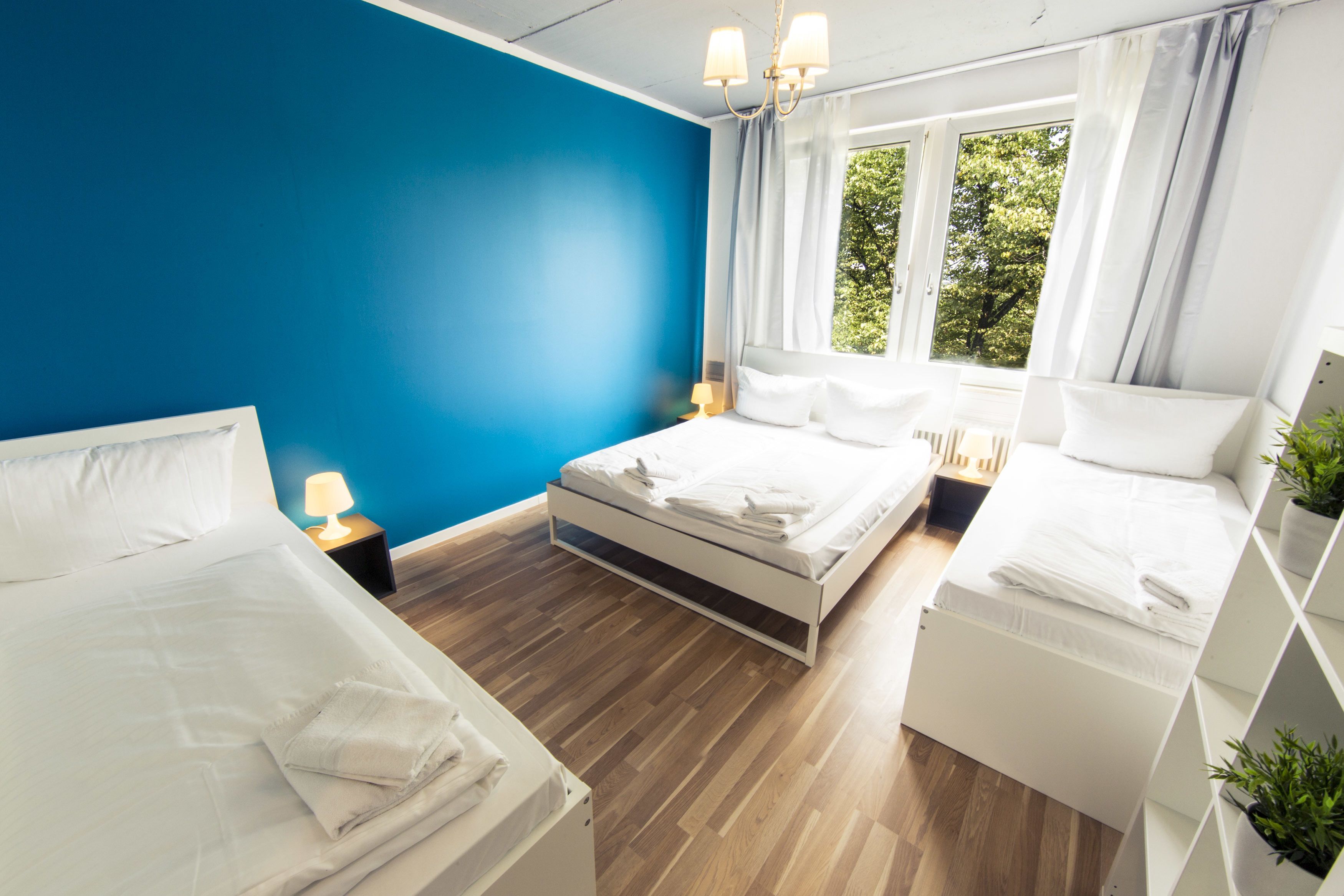 A modern hotel room with two beds, a blue accent wall, and large windows with curtains.
