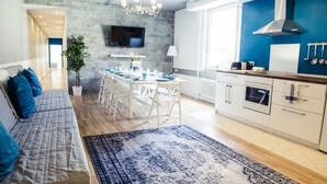 A modern kitchen with a dining area, a TV mounted on the wall, and a large window providing natural light. - Hevals Grand Tempelhof (Berlin)