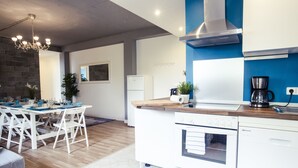 A modern kitchen with white appliances, a wooden island, and a dining area with white chairs and a table set for four. - Hevals Grand Tempelhof (Berlin)