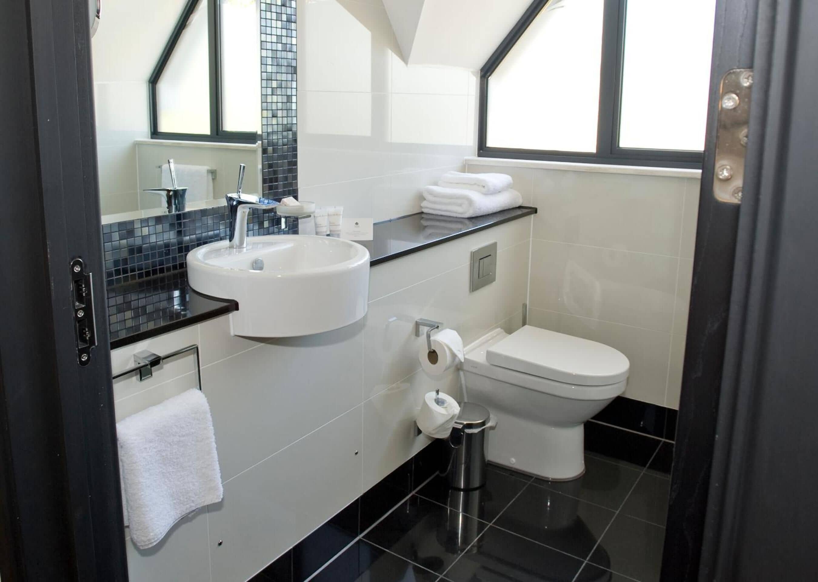 Een moderne badkamer met een witte wastafel, een zwart aanrecht en een toilet.