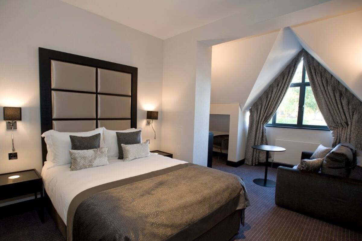 A hotel room with a large bed, a sofa, a small table, and a window with curtains.