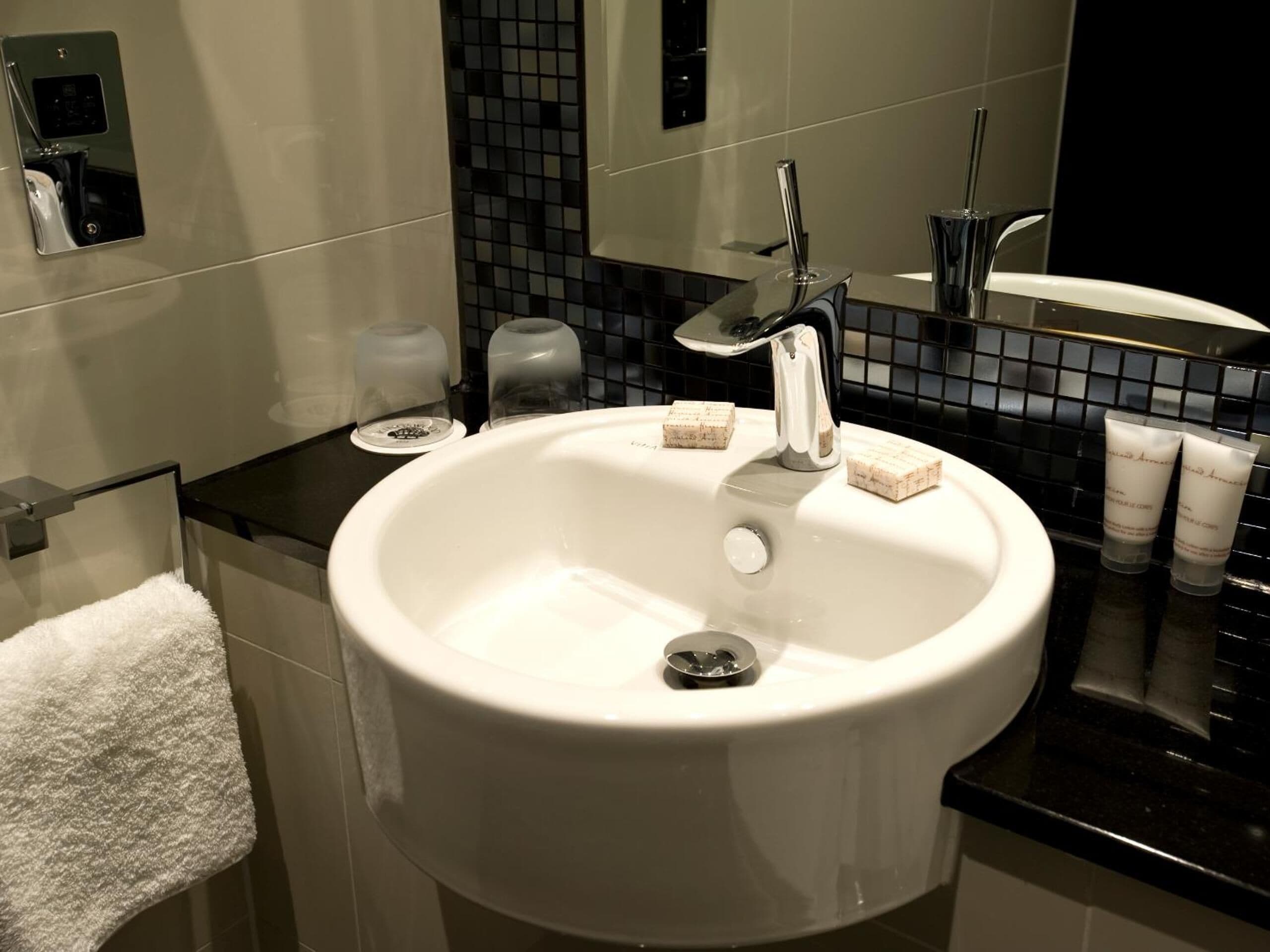 Ein modernes Badezimmer mit einem weißen Waschbecken, einer schwarzen Arbeitsplatte und einem Spiegel darüber.
