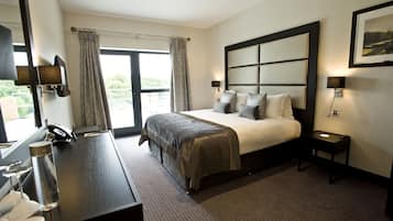 A hotel room with a large bed, a desk with a telephone, a lamp, and a window with curtains.