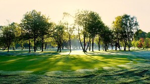 A golf course with a well-maintained green, trees, and a clear sky. - The Lodge at Kingswood (Tadworth)