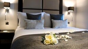 A neatly made bed with a grey bedspread, white pillows, and a decorative arrangement of white roses and petals on the bed. - The Lodge at Kingswood (Tadworth)