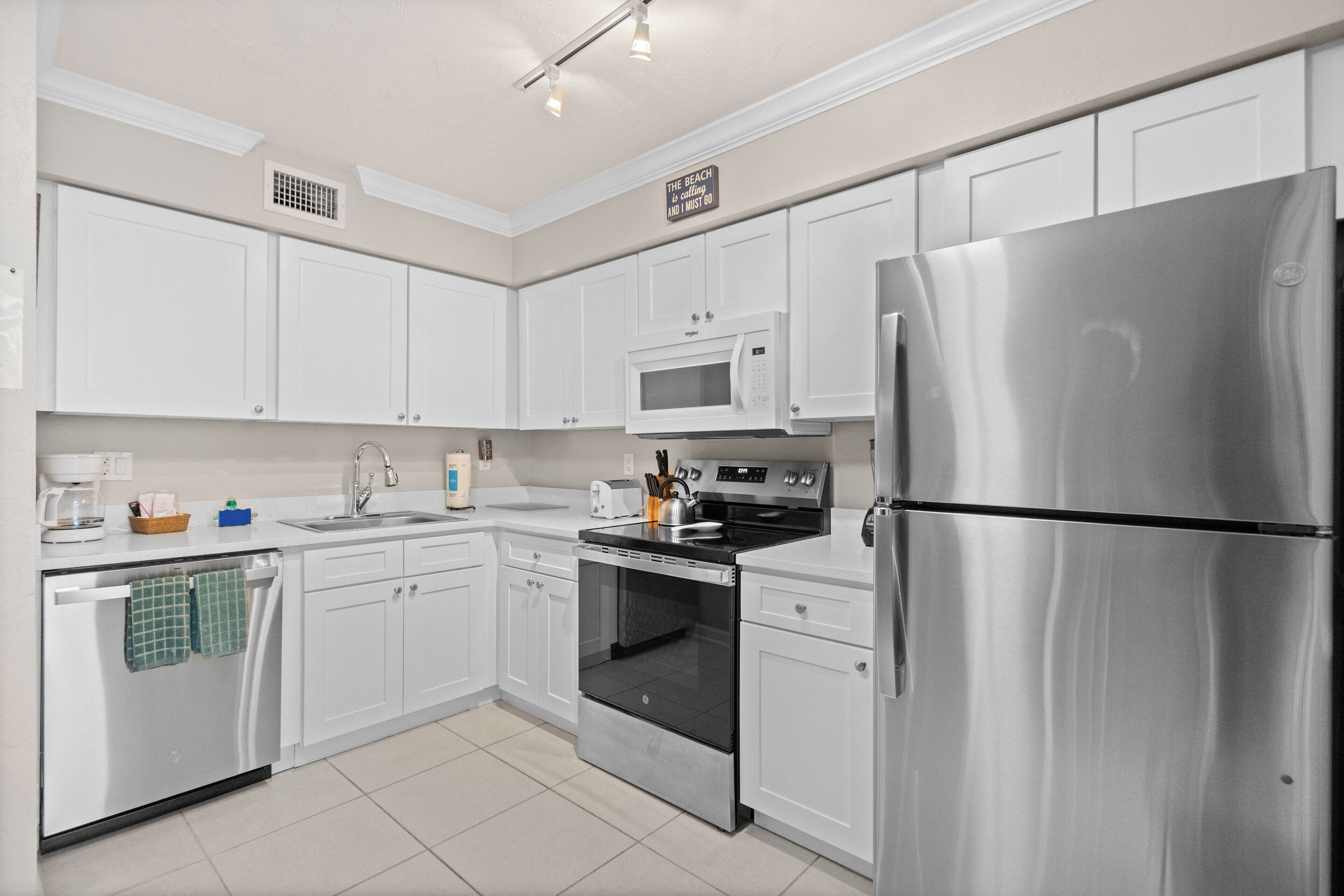 A modern kitchen with white cabinets, stainless steel appliances, and a sign on the wall.