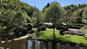 A serene riverside view with a wooden fence, lush greenery, and a clear blue sky. - Hotel Dirbach Plage (Esch-sur-Sure)