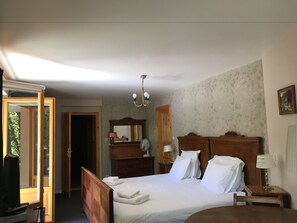 A bedroom with a wooden bed, a nightstand, a dresser, a mirror, and a chandelier. - Hotel Dirbach Plage (Esch-sur-Sure)