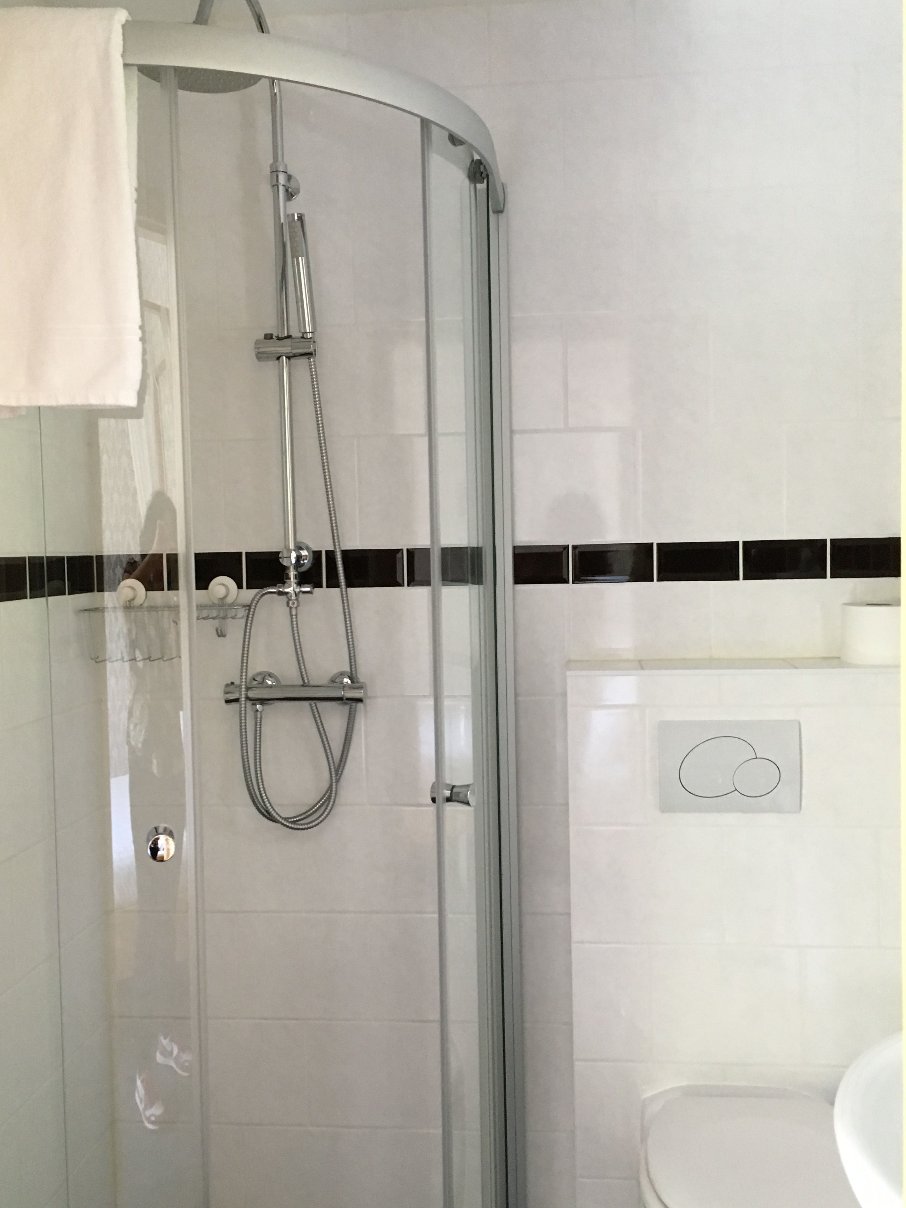 Ducha envuelta en vidrio con cabezal de ducha de mano y llave montada en la pared.
