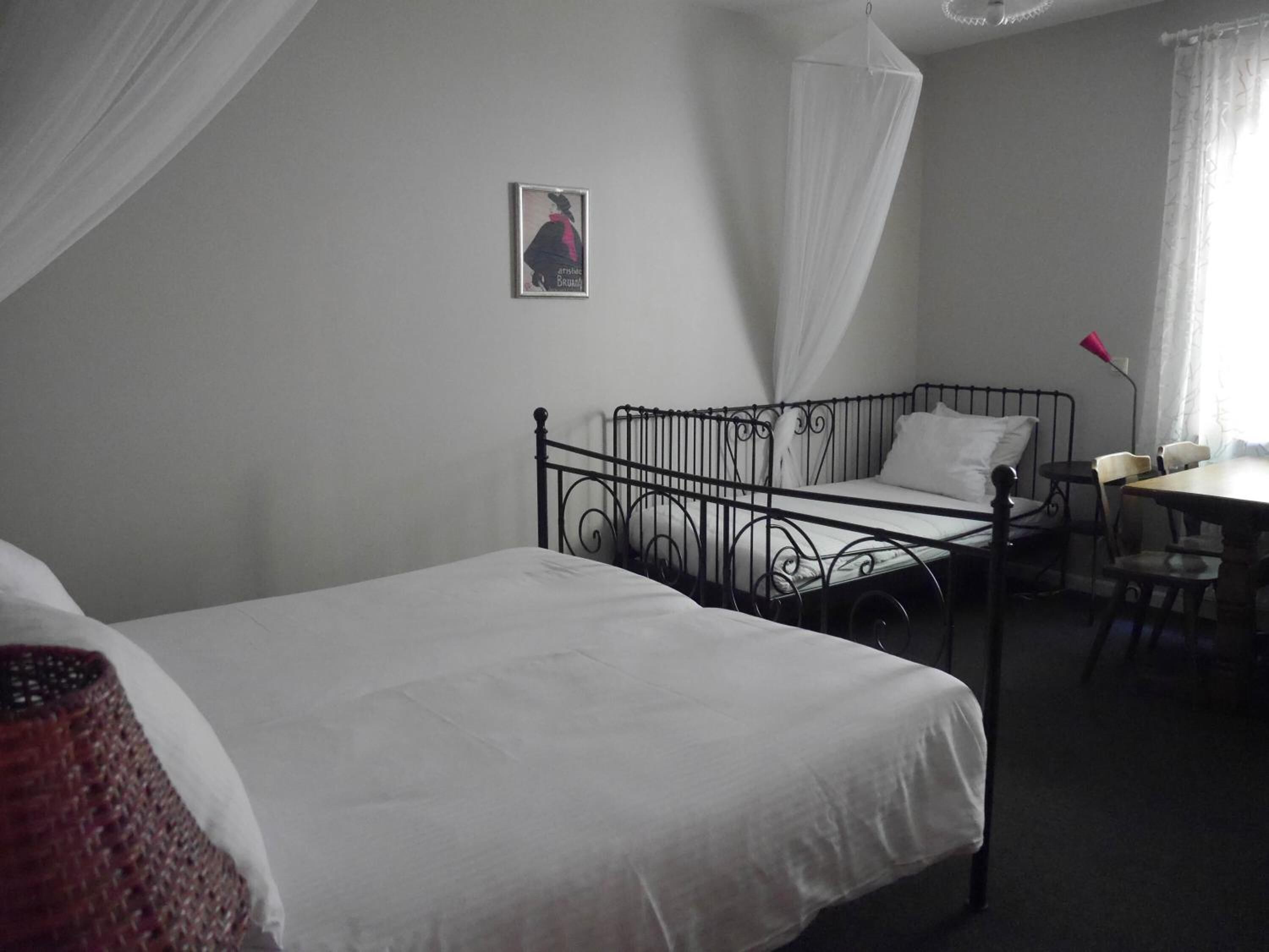 A single bed with a metal frame, a bedside table, a chair, and a small table with a lamp.