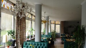 A restaurant with green upholstered booths, large windows, and hanging chandeliers. - Hotel Dirbach Plage (Esch-sur-Sure)