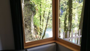 A room with a large window overlooking a forested area and a white picket fence. - Hotel Dirbach Plage (Esch-sur-Sure)