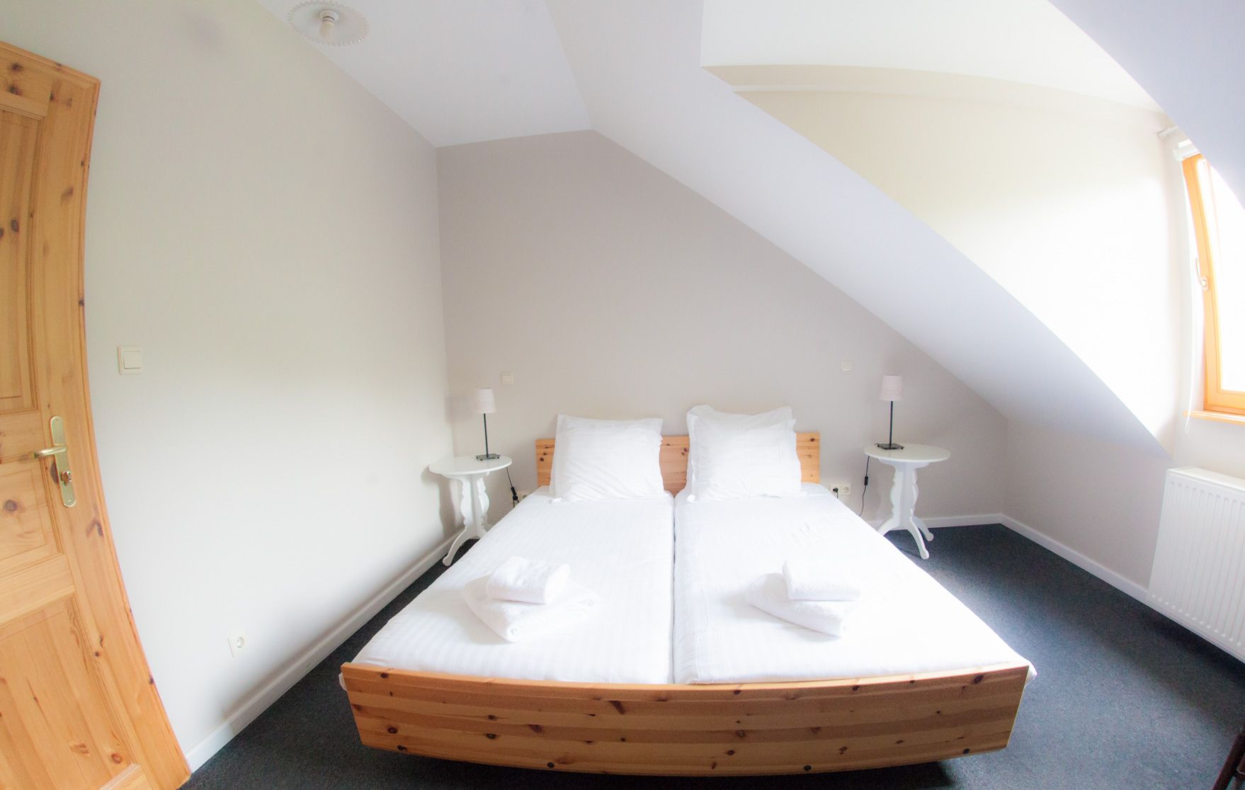 Une chambre avec un lit en bois, deux tables de chevet, une fenêtre et un plafond en pente.
