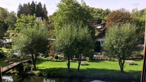 A serene riverside view with lush greenery and a wooden bridge. - Hotel Dirbach Plage (Esch-sur-Sure)
