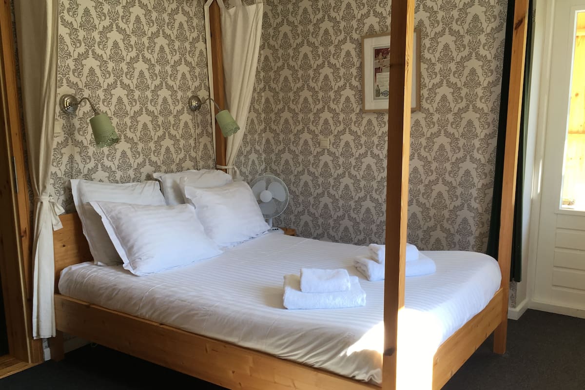 A four-poster bed with white linens and pillows, a wooden headboard, and a wall-mounted fan.