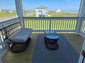 A wooden deck with a sofa and a table, overlooking a grassy area and a beach. - Kids Cottage Amazing views from all directions (Jamaica Beach)