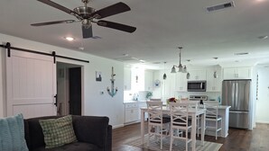 A modern kitchen with white cabinets, stainless steel appliances, and a dining area with white chairs. - Kids Cottage Amazing views from all directions (Jamaica Beach)
