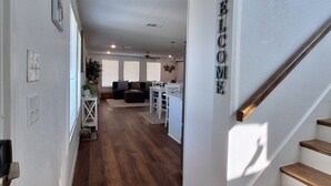 A spacious hallway with wooden flooring, a staircase with a 'WELCOME' sign, and a view into a living area with a sofa and a dining table. - Kids Cottage Amazing views from all directions (Jamaica Beach)