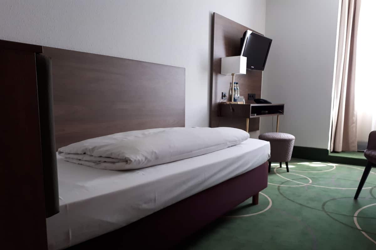 Une chambre d’hôtel comprenant un lit, un bureau avec une chaise, une télévision et un petit tabouret.