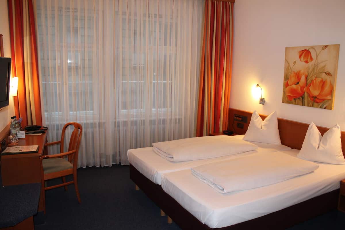 Une chambre d’hôtel avec deux lits, un bureau avec une chaise, une télévision et un tableau au mur.
