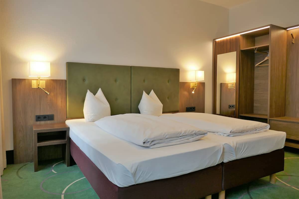 Une chambre d’hôtel avec un lit double, deux tables de chevet, une commode, une armoire et deux lampes fixées au mur.