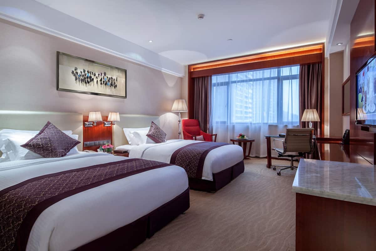 Een hotelkamer met twee bedden, een bureau, een stoel, een televisie en een raam met gordijnen.