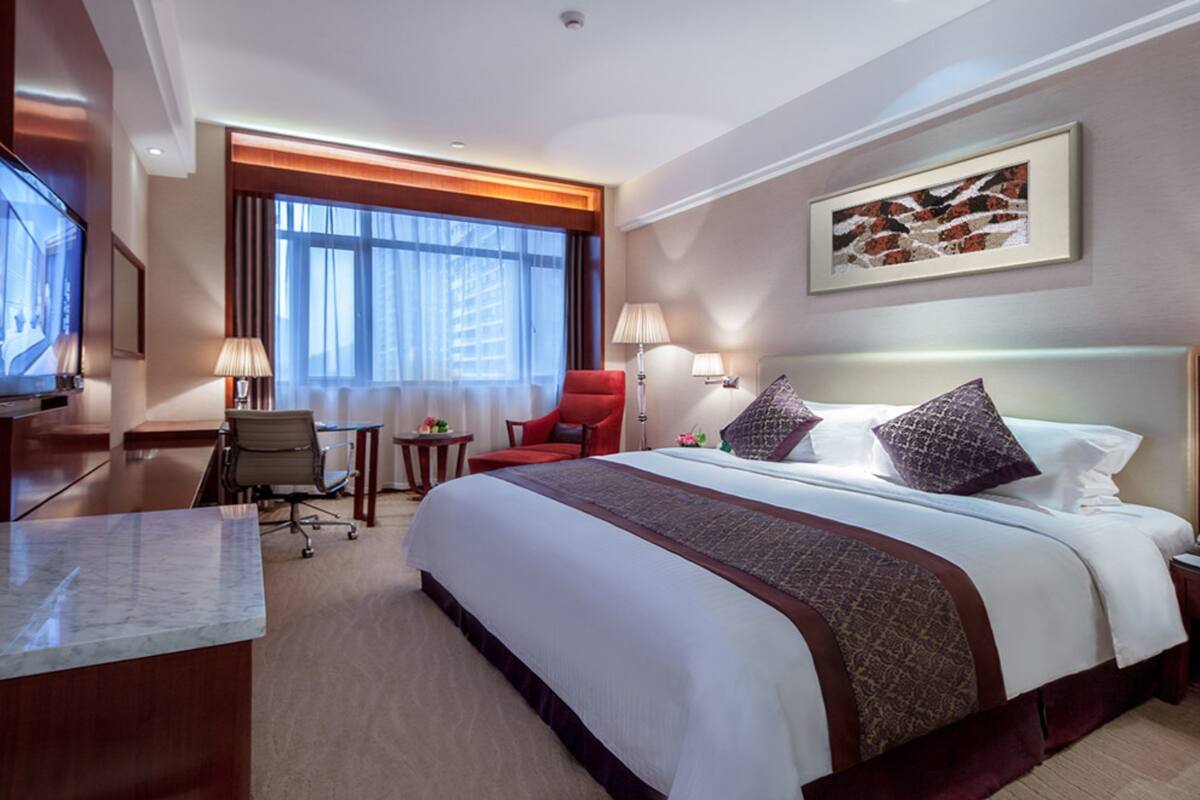 Een hotelkamer met een groot bed, een bureau met een flatscreen televisie, een stoel, een klein tafeltje en een raam met gordijnen.