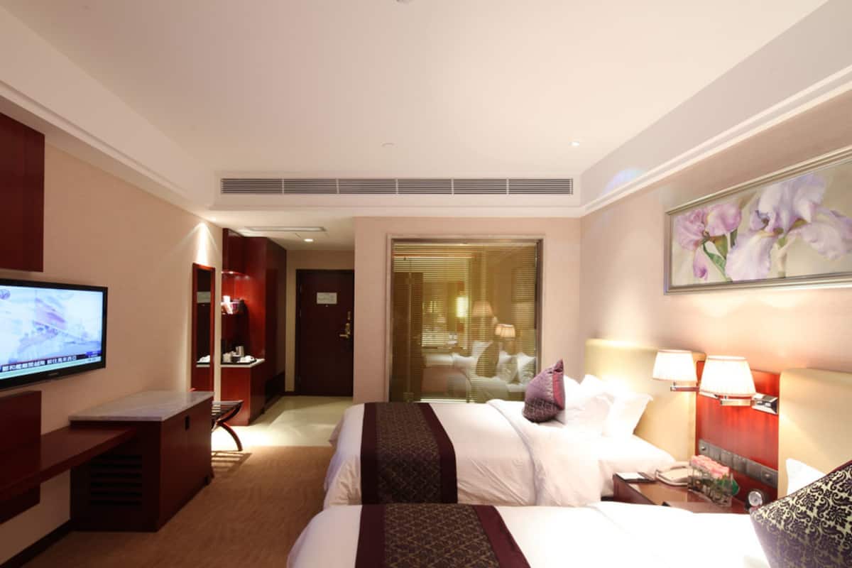 Een hotelkamer met twee bedden, een televisie, een bureau en een badkamer zichtbaar door een glazen deur.