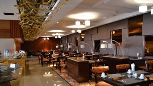 Un vestíbulo de hotel con un bar central, varias mesas de comedor y un llamativo candelabro dorado.
