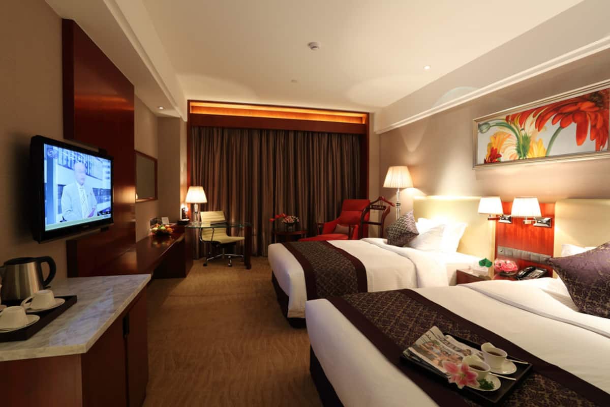 Een hotelkamer met twee bedden, een bureau met een televisie, een koffiezetapparaat en een schilderij aan de muur.