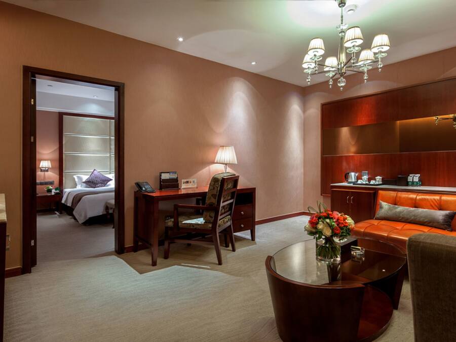 Una habitación de hotel con cama, escritorio con lámpara, zona de estar con sofá y mesa de centro.